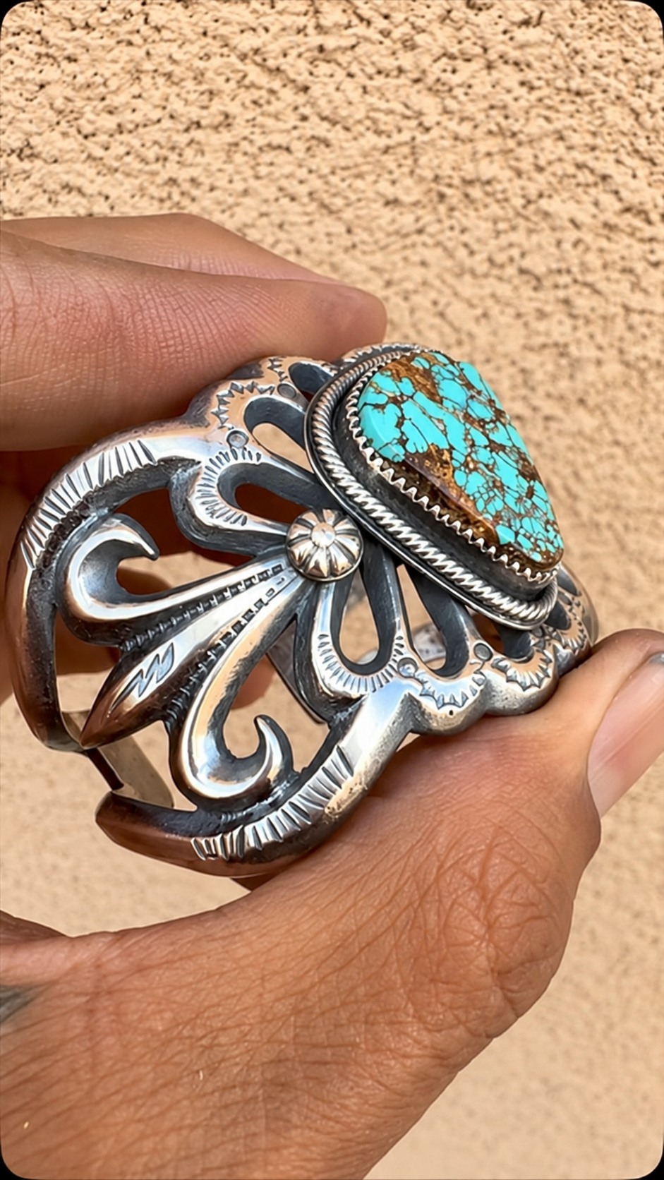Hand holding an intricately detailed silver cuff with a turquoise stone